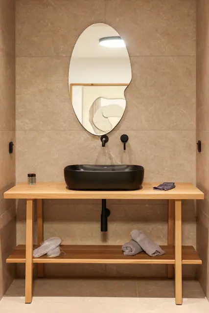 Bathroom vanity with a black basin and oval mirror on beige stone tiles