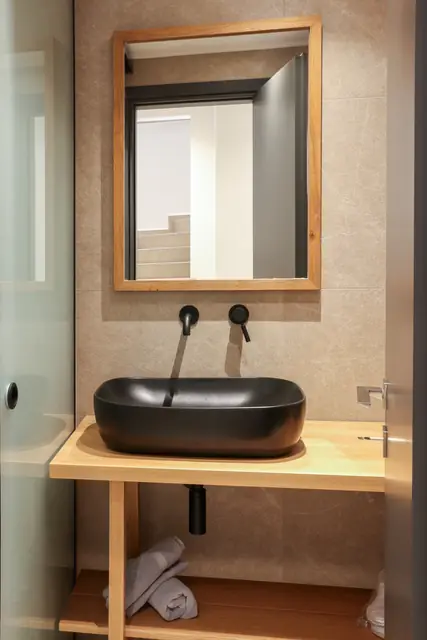 Wood-framed mirror above a black basin and wooden vanity