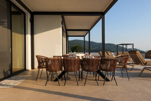 Covered terrace dining table with rattan chairs and a view toward the Ionian Sea