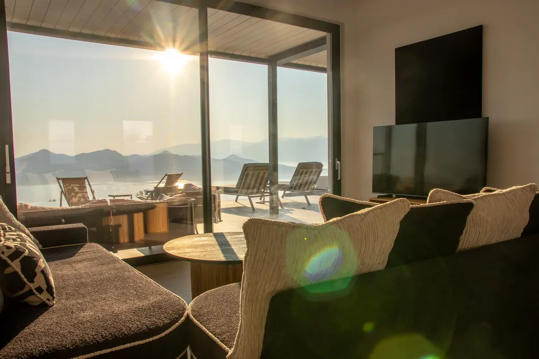 Living room in golden sunlight with a flat-screen TV and sea views
