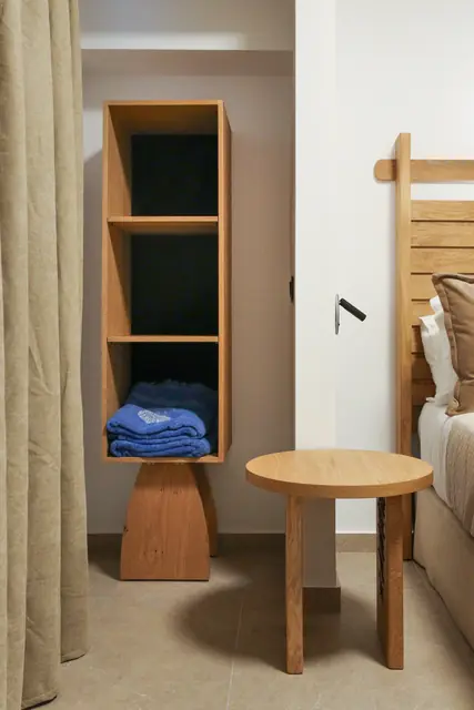 Bedroom with open wooden shelving, a side stool and linen curtains
