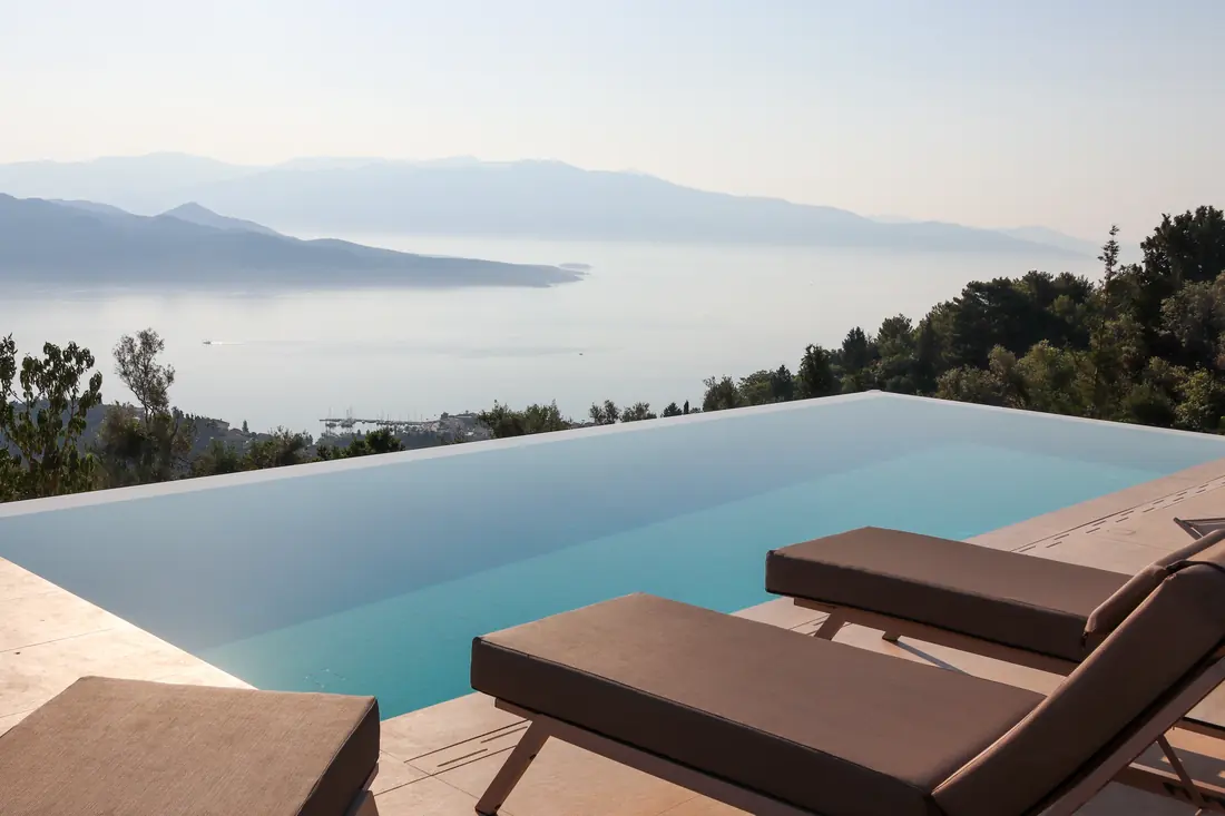 Brown sun loungers beside the pool edge with a panoramic view of the bay and mountains