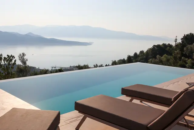 Brown sun loungers beside the pool edge with a panoramic view of the bay and mountains