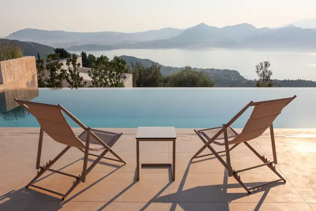 Two wooden sun loungers at the edge of the infinity pool with the Ionian Sea behind